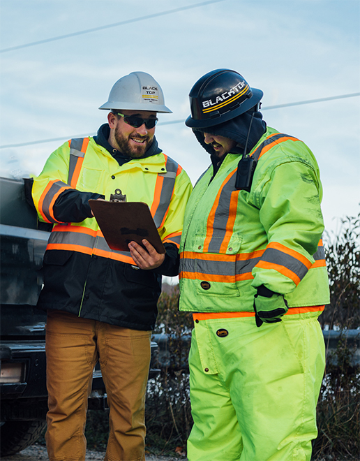 Ryan Robicheau, Owner & Operator of Blacktop Traffic Service, reviewing a traffic control plan on a clipboard with a crew member at a Nova Scotia job site